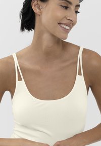 Top in crema chiaro con spalline sottili e dettagli ritagliati. Tessuto morbido ed elastico con una consistenza liscia, dotato di un'ampia scollatura.