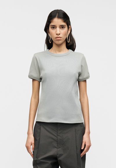 T-shirt gris clair à manches courtes avec un col rond et une texture subtile, associé à un pantalon ample de couleur foncée, présentant un design simple.