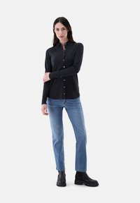 Schwarze Button-Up-Bluse mit Kragen und langen Ärmeln, kombiniert mit hellblauen geraden Jeans und schwarzen Knöchelstiefeln. Glatte Textur.