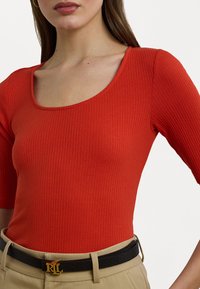 Κόκκινη ριγέ μπλούζα με τετράγωνη λαιμόκοψη και κοντά μανίκια, συνδυασμένη με ζώνη σε χακί τόνο που διαθέτει χρυσή λεπτομέρεια.