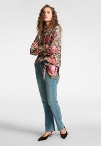 Top marrón con estampado floral y acentos rosas, atado de lado; combinado con jeans rectos de mezclilla azul claro y zapatos de tacón tipo slingback marrones.