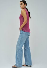 Fuksijasti pleteni top s labavim krojem i teksturiranim dizajnom, u kombinaciji sa svijetlop Plavim širokim trapericama i crnim sandalama na remen.