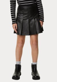 Falda de cuero negra con pliegues y cintura alta, combinada con botas negras hasta el tobillo y calcetines grises. Rayas horizontales visibles en la parte superior.