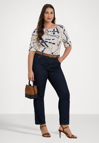 Bela majica z mornarsko modrim abstraktnim vzorcem, temno modri jeans, rjav pas in mala dvobarvna torbica. Rjave sandale z vezalkami zaokrožajo obleko.