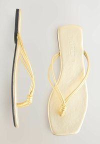 Sandali infradito oro con un design piatto. Materiale morbido e lucido con cinturini sottili e un dettaglio annodato, suola in gomma nera.