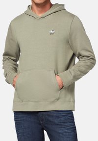 Hoodie w kolorze oliwkowym z bawełnianej mieszanki, posiada kieszeń z przodu oraz haftowane logo. Rybkowane mankiety i dół dodają faktury.