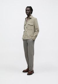 Khaki corduroy overhemd met twee borstzakken, gecombineerd met lichtgrijze broek en bruine leren schoenen. Eenvoudig, gestructureerd ontwerp en een ontspannen pasvorm.