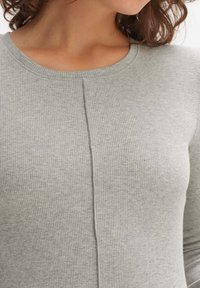 Gray ribbed long-sleeve top with a rounded neckline and a central seam detail, made from a soft, textured fabric.