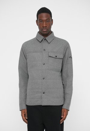 Harmaa tikattu takki, jossa on kaulus, etutasku ja nepparit. Valmistettu villasekoitekankaasta, jossa on sileä rakenne ja hienoinen kiilto.