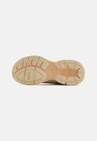 Shoe sole with a beige rubber outsole featuring treads and grooves for traction, embossed brand name, and a smooth tan midsole section.