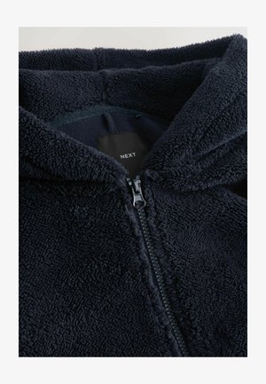 Granatowa polarowa bluza z kapturem o teksturowanej, puszystej powierzchni, z przodu na zamek błyskawiczny i czarną metką z nazwą marki "NEXT" wewnątrz kołnierza.