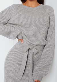 Femme portant une robe en tricot côtelé gris clair avec de longues manches bouffantes et une ceinture nouée à la taille.