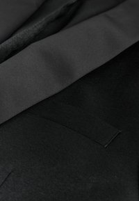 Black jacket featuring smooth fabric, a textured interior, and a subtle pocket detail. The design is minimalist and tailored.