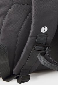 Sac à dos en tissu noir avec un matériau texturé, des bretelles ajustables et un logo blanc. Comprend des accessoires solides et des coutures renforcées.