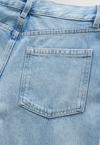 Poche arrière sur un jean en denim bleu clair avec des coutures visibles et une passants de ceinture à la taille.