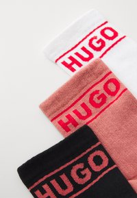 Tre par sokker i hvit, rosa og svart, hver med rødt "HUGO"-merke på den øverste kanten. Teksturert stoff med ribbede detaljer.