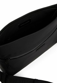 Sort crossbody-tasker lavet af glat materiale, med lynlåslukning og prægning af logoet på forsiden. Justerbar rem inkluderet.