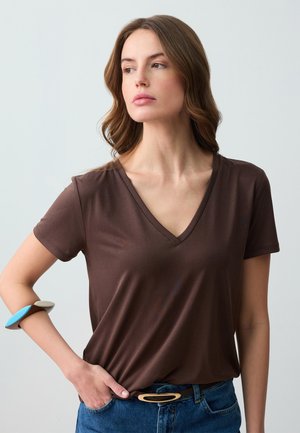 T-shirt à col en V marron en tissu doux avec des manches courtes, associé à un jean bleu et une ceinture décorative avec un accent beige et bleu.