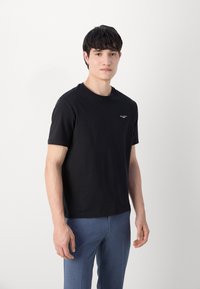 Zwarte katoenen t-shirt met korte mouwen, ronde hals, aansluitend ontwerp, voorzien van een klein wit logo op de bovenste linkerkant van de borst.