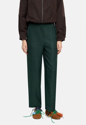 Zielone, teksturowane spodnie o szerokich nogawkach z wysokim stanem. Noszone z brązową kurtką na suwak i brązowymi butami z kolorowymi, ozdobnymi sznurowadłami.