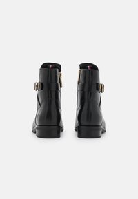 Botas de cuero negro hasta el tobillo con forma afinada, cremalleras laterales y hebillas doradas. Presentan un material texturizado y un diseño de tacón bajo.