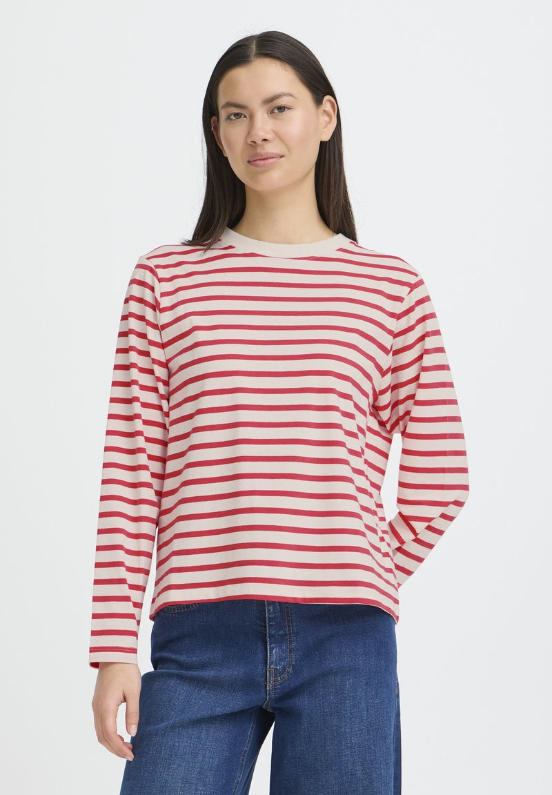 Chemise à manches longues rayée rouge et blanche avec un col rond, fabriquée en tissu doux. Coupe ample, associée à un jean bleu foncé.