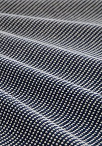 Marine blauwe stof met een wit stippenpatroon, gestructureerde weefsel en een lichte golfbeweging. Het materiaal lijkt zacht en flexibel, geschikt voor verschillende toepassingen.