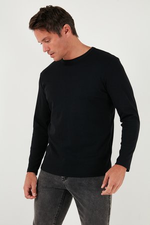 T-shirt nera a maniche lunghe in un tessuto morbido e leggero, con scollatura a girocollo e silhouette aderente, indossata con jeans in denim grigi.