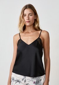 Camisole en satin noir avec des bretelles ajustables, un décolleté en V et de délicates accents en dentelle sur les épaules. Texture lisse avec une coupe décontractée.