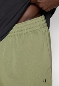 Ανοικτό πράσινο παντελόνι τζόγκινγκ από μαλακό ύφασμα, με ελαστική μέση και πλαϊνές τσέπες, καθώς και λεπτομέρεια λογότυπου στο κάτω μέρος του ποδιού.