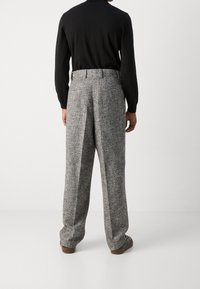 Pantaloni in tweed grigio con vestibilità ampia e cuciture verticali evidenti. Abbinati a una maglia nera aderente a maniche lunghe.