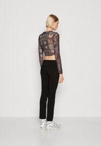 Top scurt negru din plasă cu modele de inimă, asortat cu pantaloni negri ajustați și adidași albi cu litere îndrăznețe.