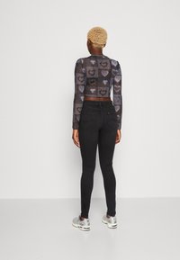 Svarta högmidjade skinny jeans med en slät textur. Kombinerat med en genomskinlig långärmad topp med ett hjärtmönster i nyanser av grått.