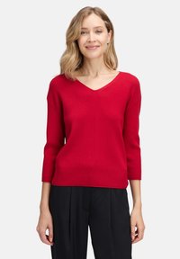 Roter gerippter Strickpullover mit V-Ausschnitt und Dreiviertelärmeln, der ein figurbetontes Design und eine einheitliche Farbe aufweist.
