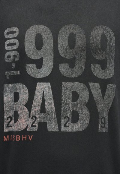 Μαύρο ύφασμα με φθαρμένο γκρι κείμενο «999 BABY» και μικρότερα αλφαριθμητικά στοιχεία, συμπεριλαμβανομένων των «T-9000» και «MISBHV» σε κόκκινο.
