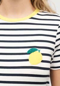 Λευκό και ναυτικό ριγέ πουκάμισο με κίτρινο γιακά και κεντημένο κίτρινο λεμόνι με πράσινο φύλλο στο στήθος.