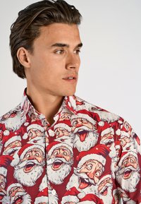 Rode katoenen shirt met een herhalend patroon van cartoon Santa Claus gezichten met witte baarden en rode hoeden. Spitse kraag en knopen zichtbaar.