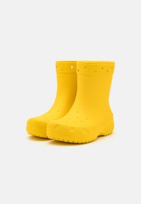 Une paire de bottes en caoutchouc étanches de couleur jaune vif avec des semelles texturées et des trous de ventilation, présentée sur un fond blanc uni.