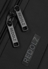 Sac en tissu noir avec surface texturée. Deux fermetures éclair avec "REDOLZ" gravé en noir. Une étiquette est également présente, assortie au schéma de couleurs.
