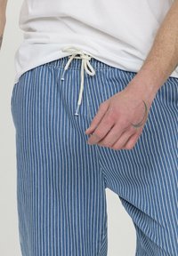 Pantalon rayé bleu et blanc avec une taille à cordon, présentant une texture de tissu douce, une coupe décontractée et des détails de couture visibles.