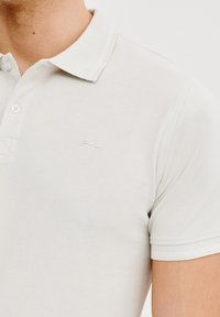 Biała koszulka polo z krótkim rękawem, wykonana z teksturowanej bawełny, z dwiema guzikami przy dekolcie oraz subtelnym, wyhaftowanym logo na piersi.
