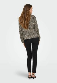 Blusa a fantasia zebra beige e nera, maniche lunghe, vestibilità comoda. Abbinata a jeans skinny neri e tacchi a spillo neri.