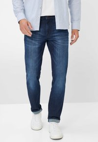 Donkerblauwe denim jeans met een rechte snit, met een subtiele textuur en lichte vervaging. Gedragen met opgerolde boorden en witte sneakers.