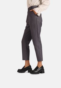Pantaloni grigi su misura con gamba affusolata e tasche laterali, abbinati a eleganti mocassini neri con tacco alto e suola strutturata.
