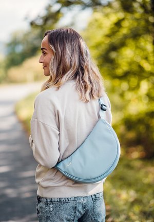 Himmelblaue, geschwungene Umhängetasche aus glattem Material; mit verstellbarem Tragegurt und dezentem Logo-Detail. Wird über die Schulter getragen.