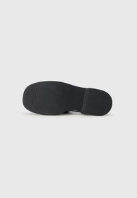 Zwarte rubberen schoenzool, plat met een textuur en geometrisch patroon. Iets breder bij de hiel en taps toelopend naar de voorkant.