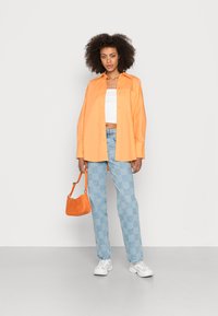 Camisa oversized laranja com botões, top cropped branco, jeans em padrão xadrez azul claro, bolsa laranja e ténis brancos. Texturas planas e lisas.