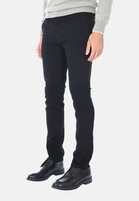 Jeans neri slim-fit in denim, con tasche frontali, cuciture sottili e una texture liscia, abbinati a scarpe eleganti nere.