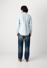 Light blue striped button-up shirt with a curved hem, paired with loose, faded blue jeans and brown shoes, viewed from the back.
