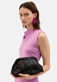 Czarna torebka kopertówka z iryzującym nadrukiem zwierzęcym, o miękkiej teksturze i zaokrąglonym kształcie, trzymana przez osobę ubraną w różową sukienkę bez rękawów.